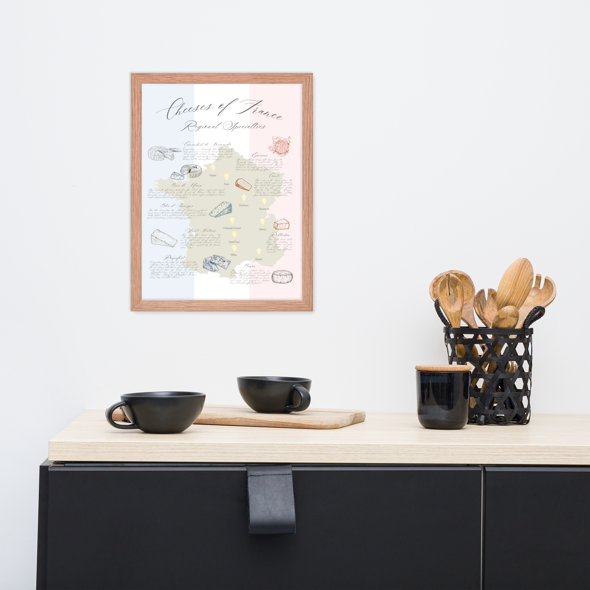 French cheese map art print in a natural wooden frame hanging above a table with cups and wooden kitchen tools.