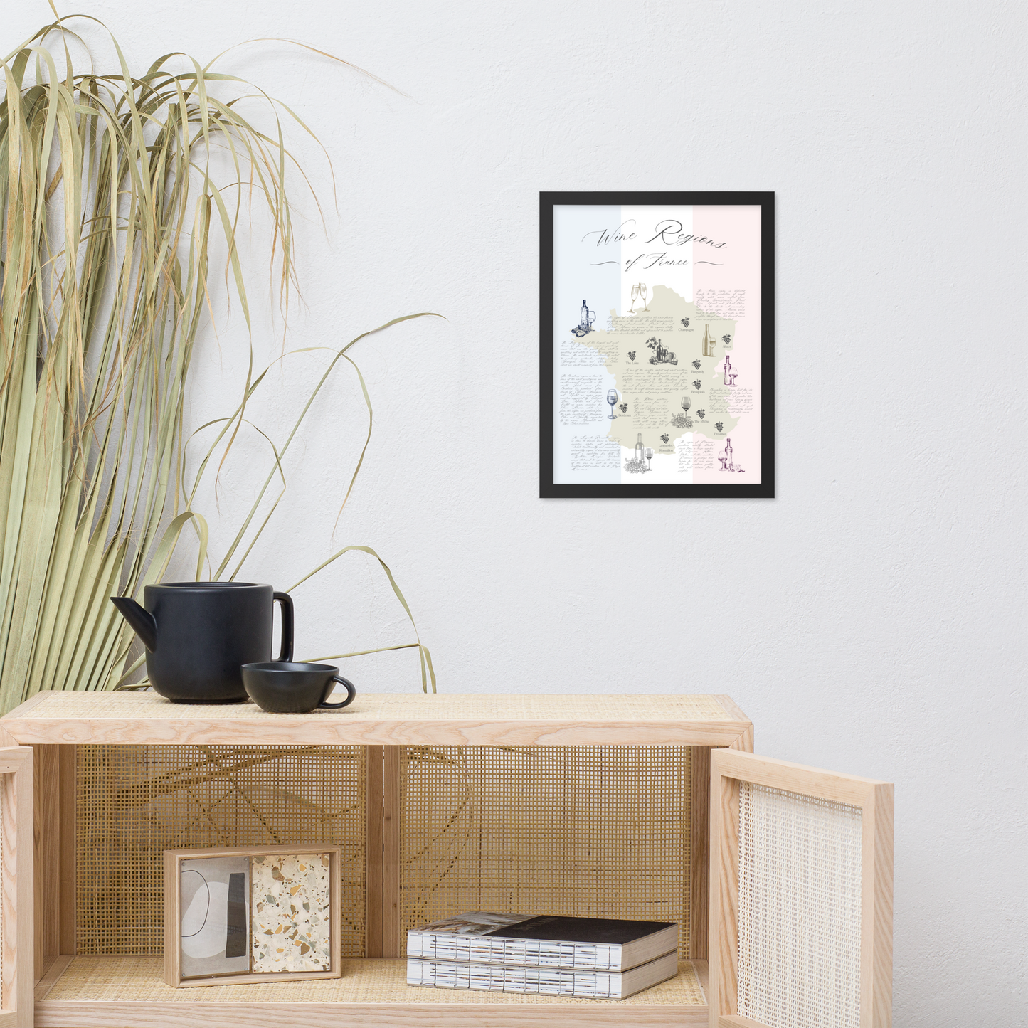 French wine map art print in a black wooden frame hanging above a sideboard with teapot and teacups.